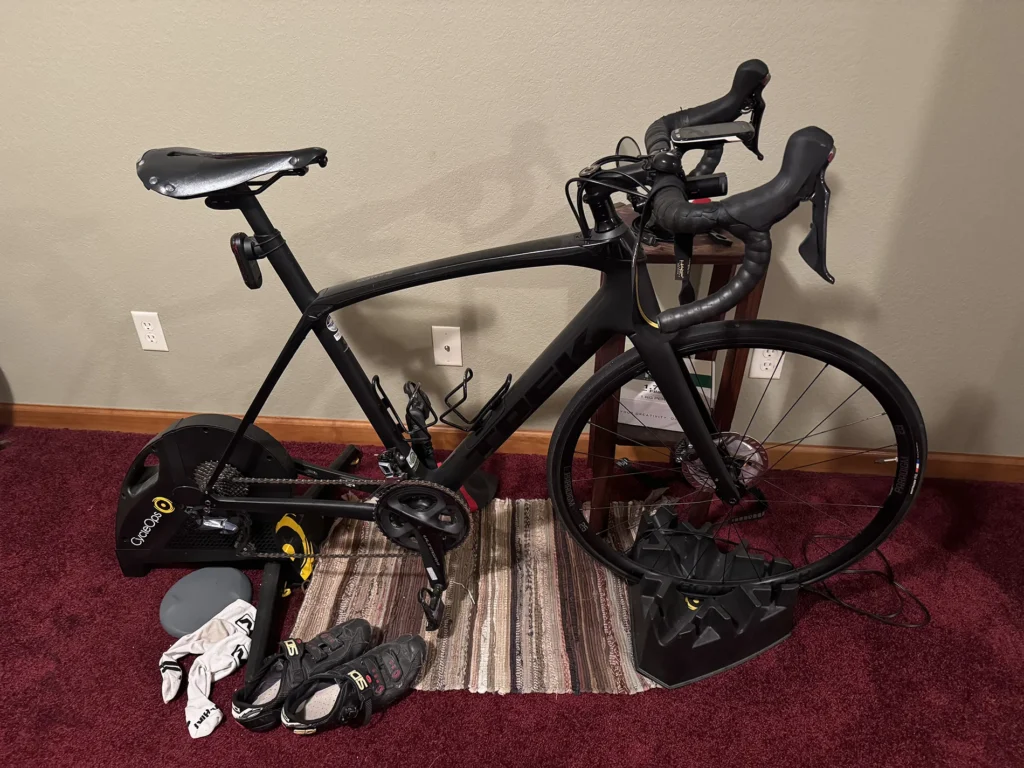 Trek Domane SL on a CycleOps indoor trainer in a basement with cycling shoes on the floor